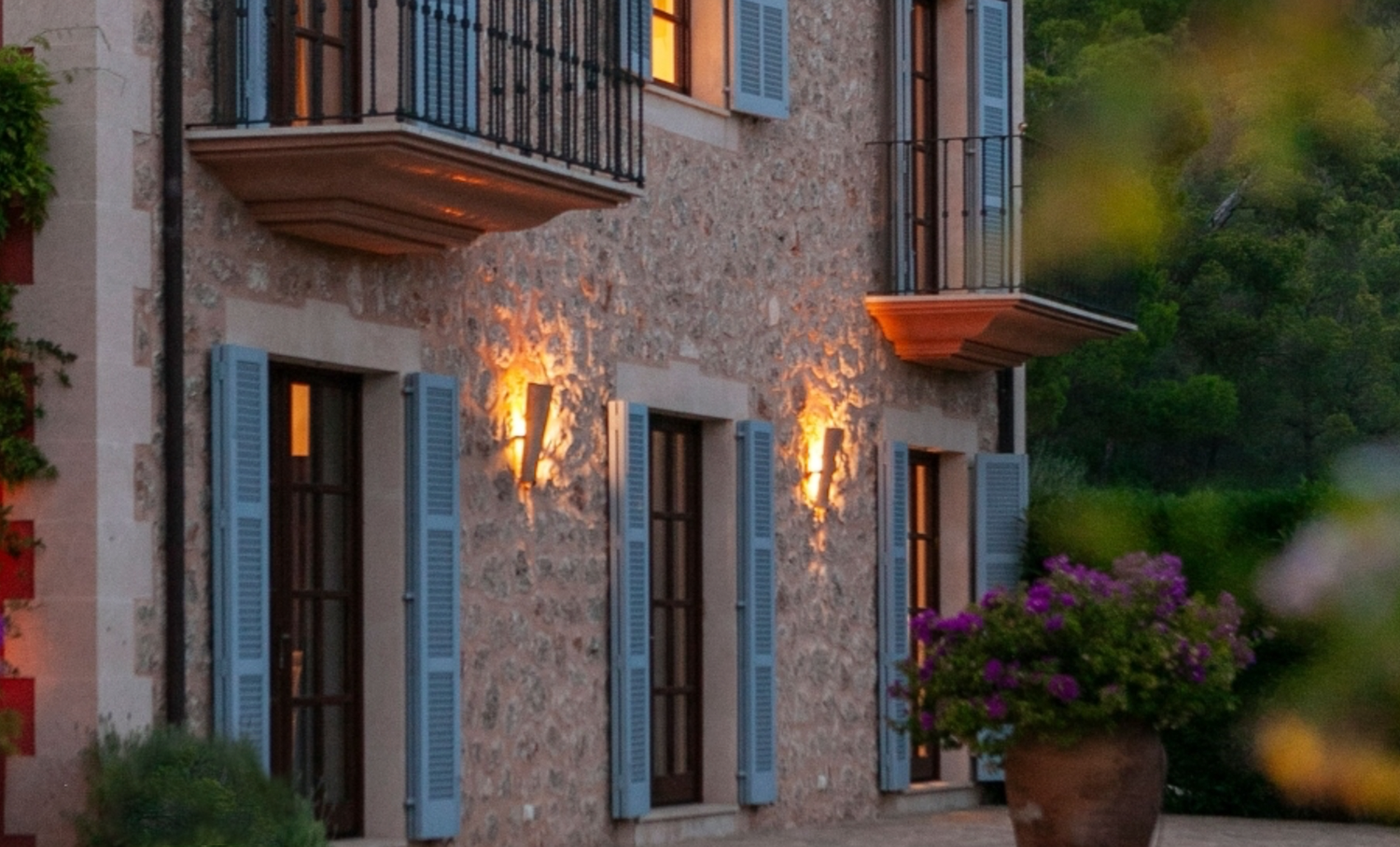 Close-up of villa exterior with blue shutters and decorative wall sconces at twilight.