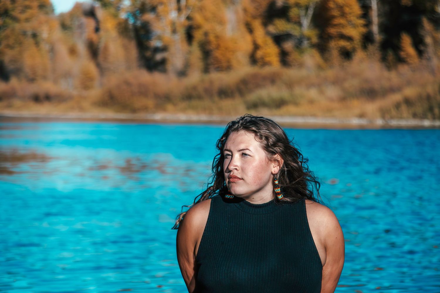 A scenic portrait shot against vibrant turquoise water and autumn trees.