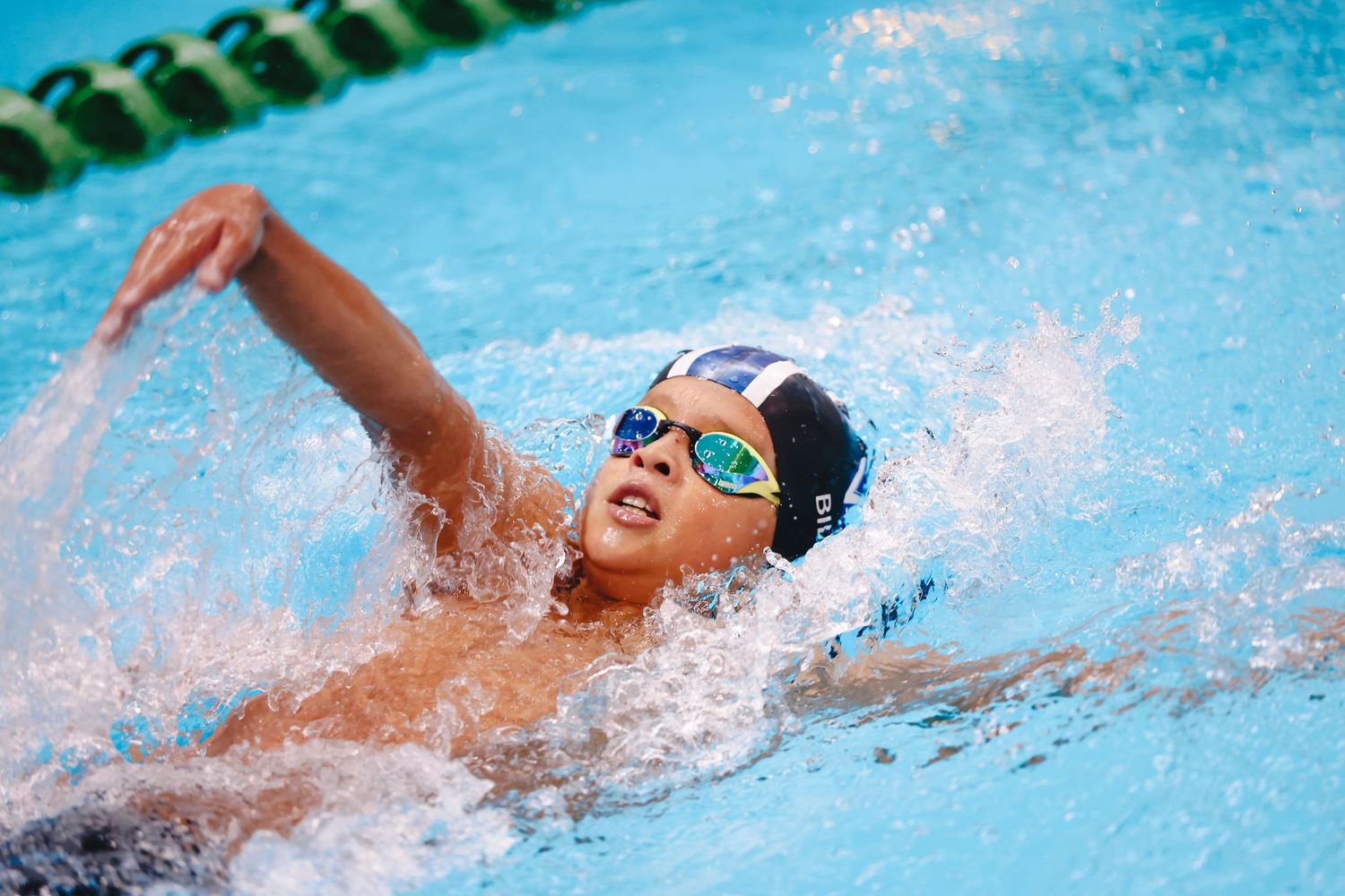 Swimmer performing backstroke in clear blue swimming pool with splashing water.