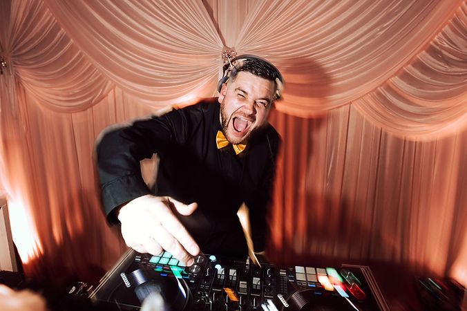 DJ performing at a party venue with draped curtains behind the turntables and dramatic lighting. SweetVibe Events