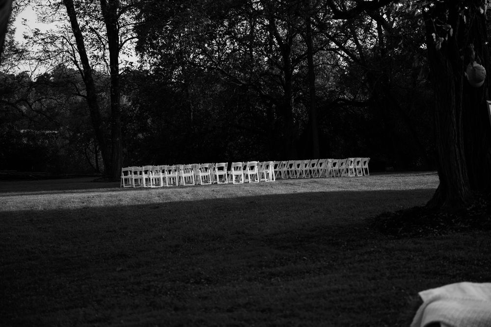 Rows of empty white chairs arranged on a lawn for an outdoor ceremony in black and white.