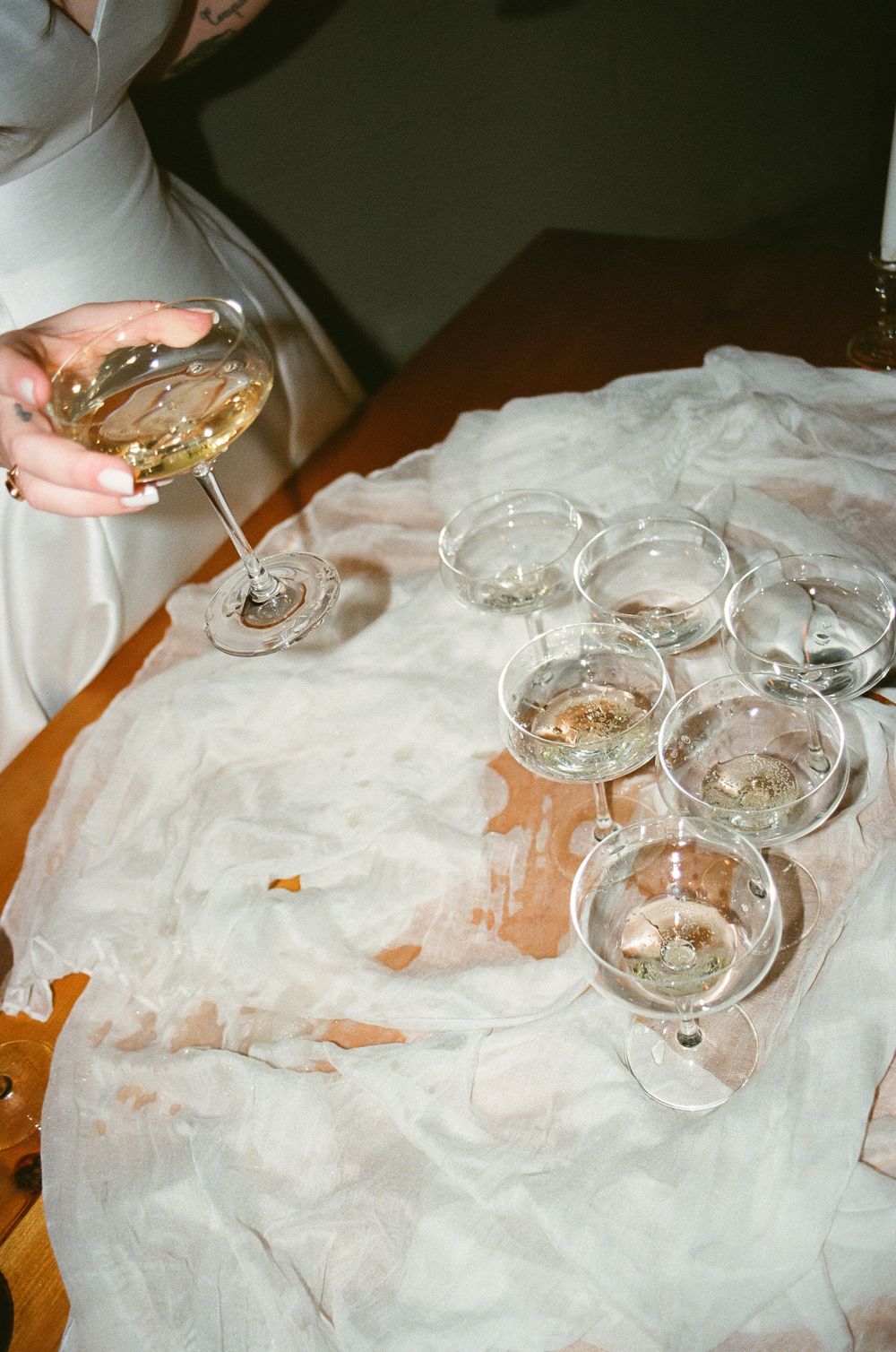 Several empty champagne glasses arranged on a white tablecloth with someone pouring a drink into one glass.