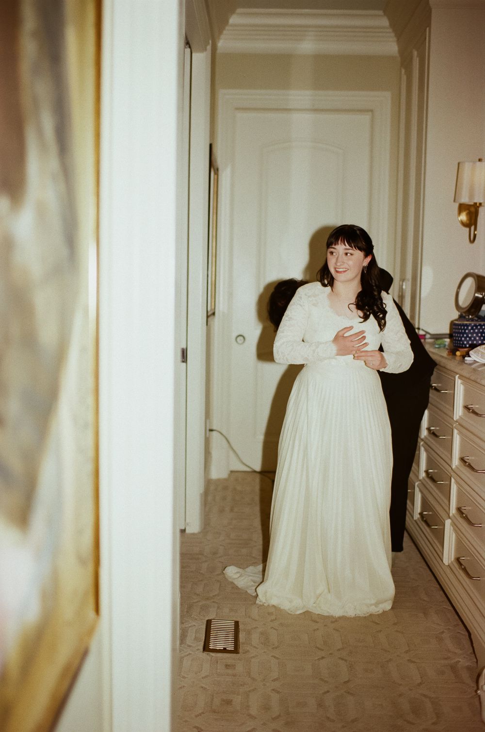 A guest appears in a vintage-style white wedding dress standing in an elegant hallway with patterned carpet.