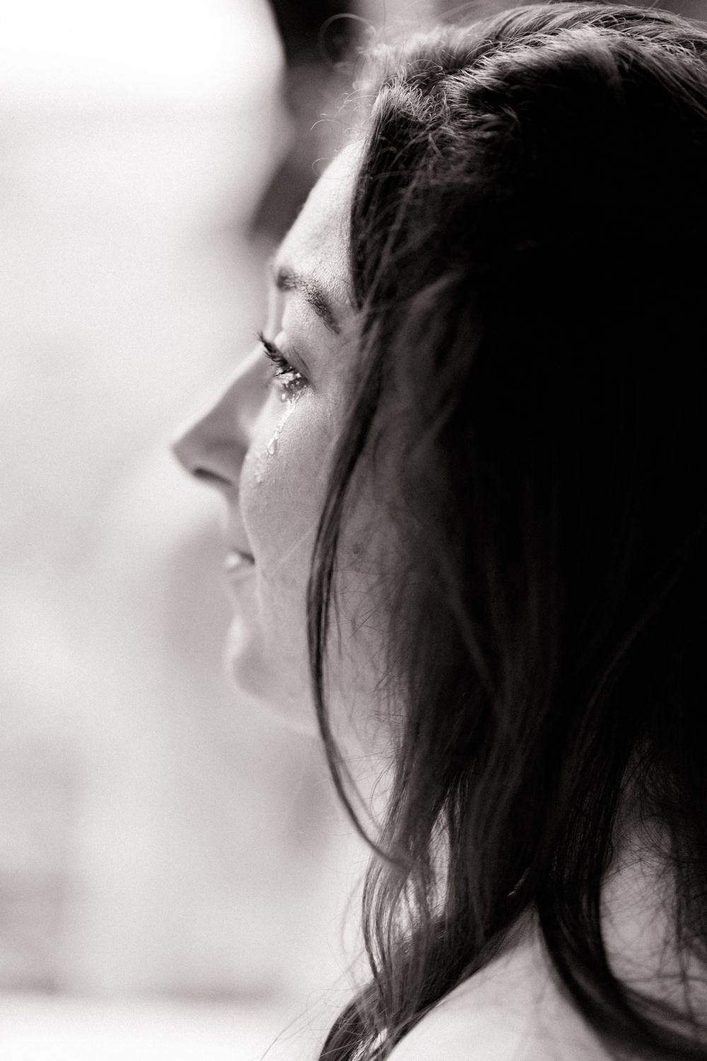 Black and white profile portrait of a woman with tears streaming down her face, capturing a deeply emotional moment.