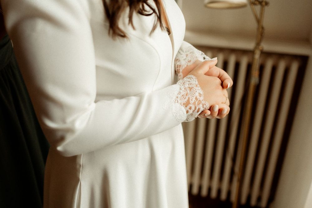 Bride in white long-sleeve lace wedding dress with hands clasped together in elegant pose.