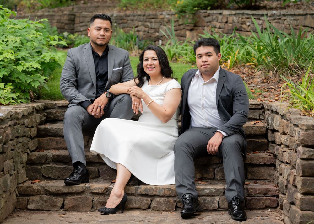 polished family portrait at birmingham botanical gardens. woman in white dress, son and husband in grey suites. all sitting on stone steps
