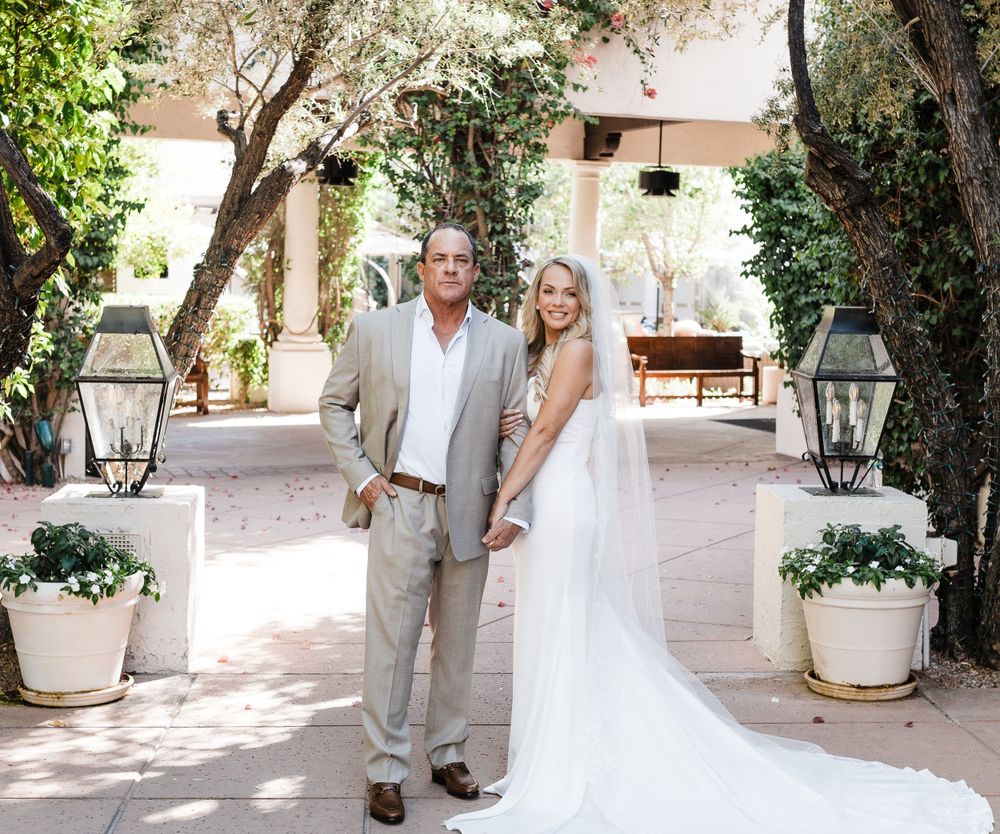Wedding couple poses in a sunlit courtyard with hanging lanterns and potted plants.