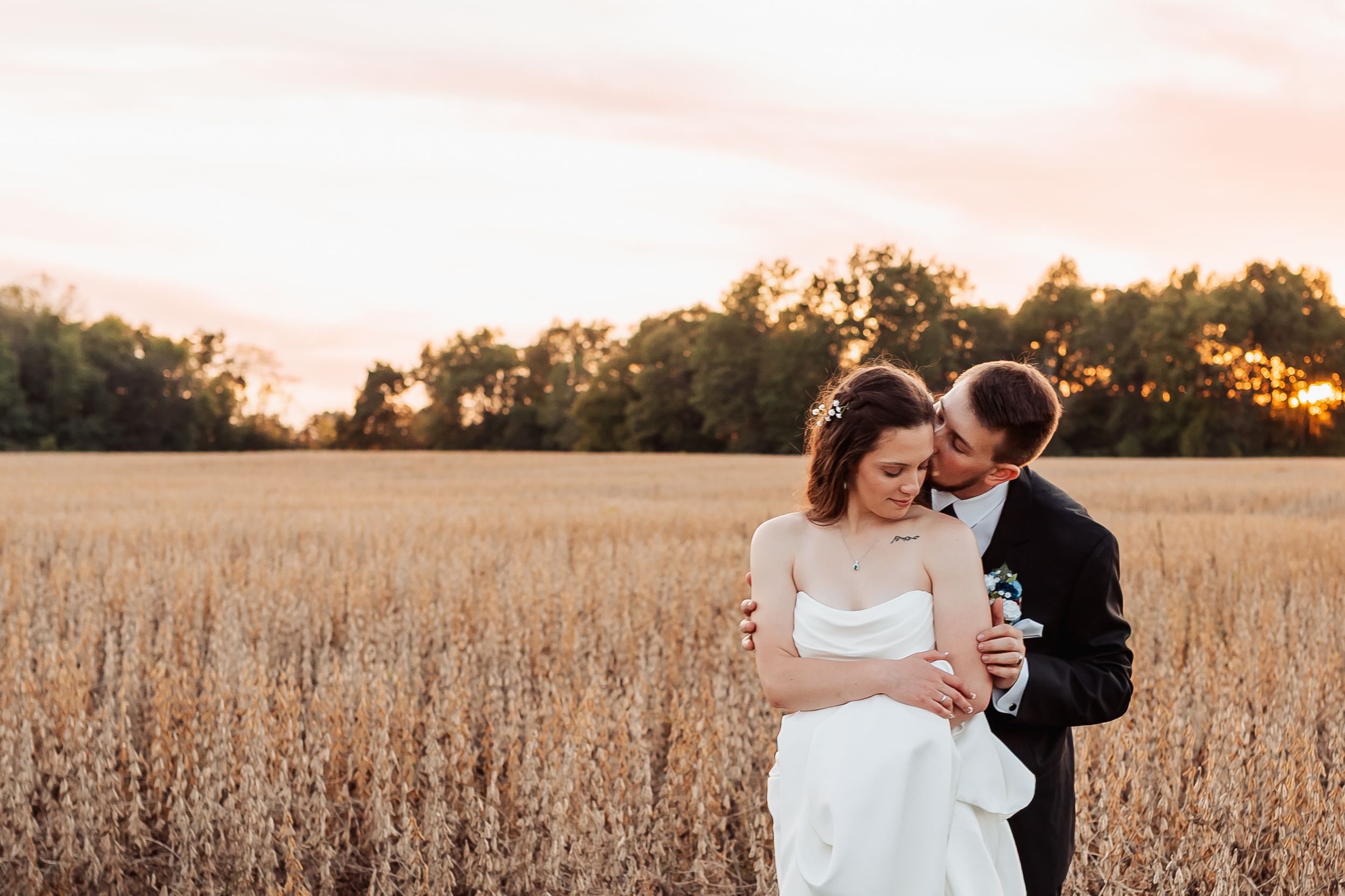 Bride and groom embracing in a golden wheat field during a beautiful sunset on their wedding day.