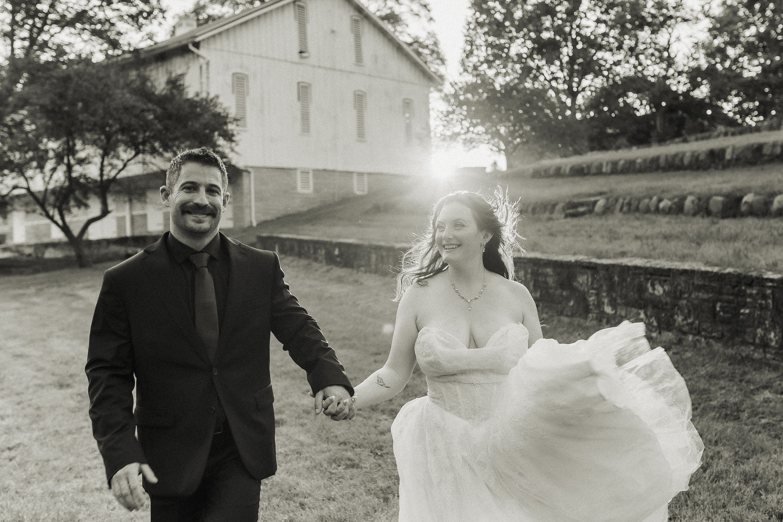 Black and white photo of a smiling bride and groom holding hands outdoors near a historic building on their wedding day.