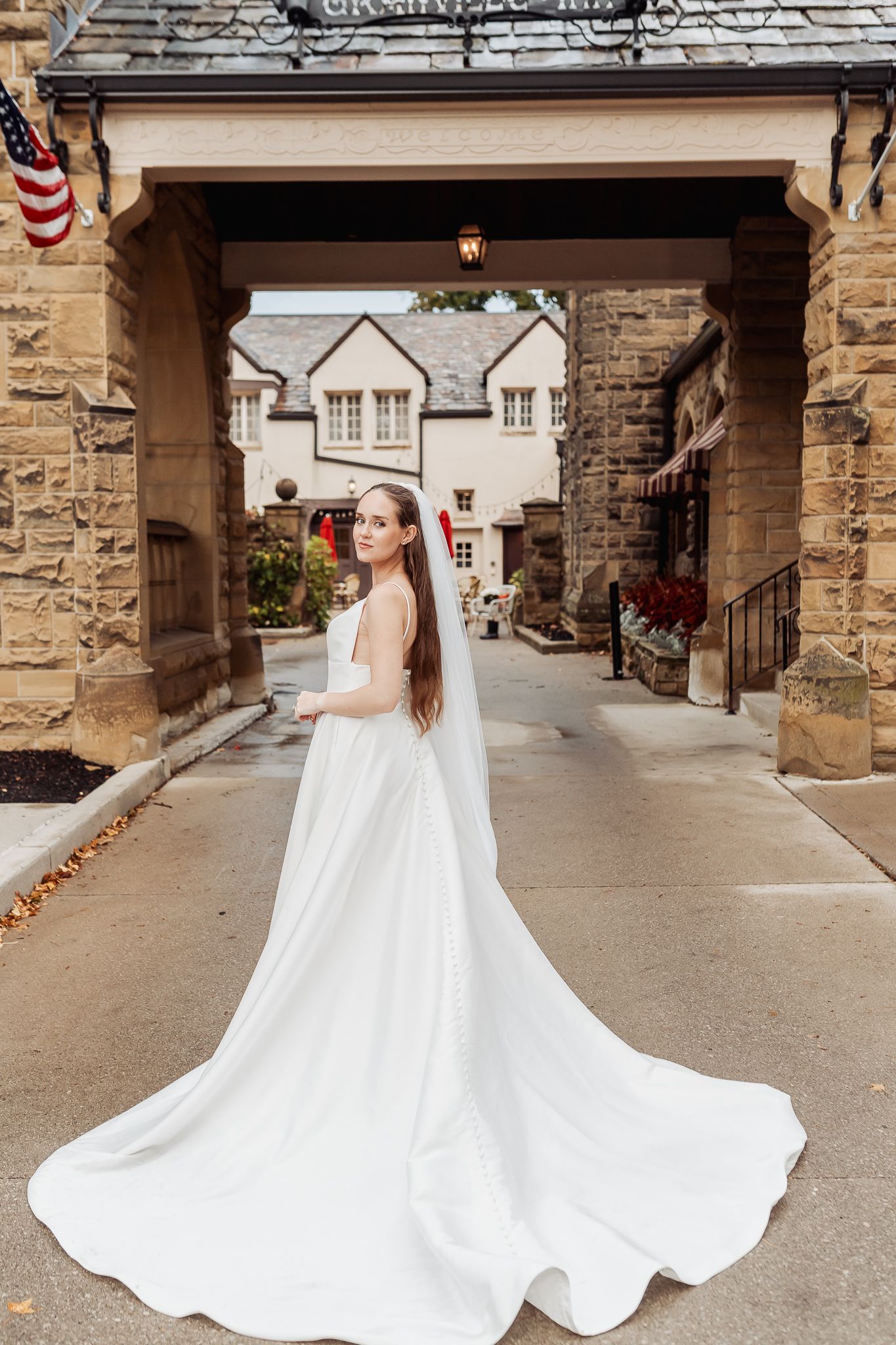 Bride in elegant white gown with long veil poses under stone archway at Granville Inn wedding venue.