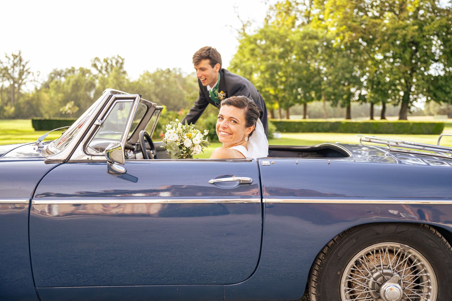 Classic blue convertible car photographed outdoors in a sunny park setting.