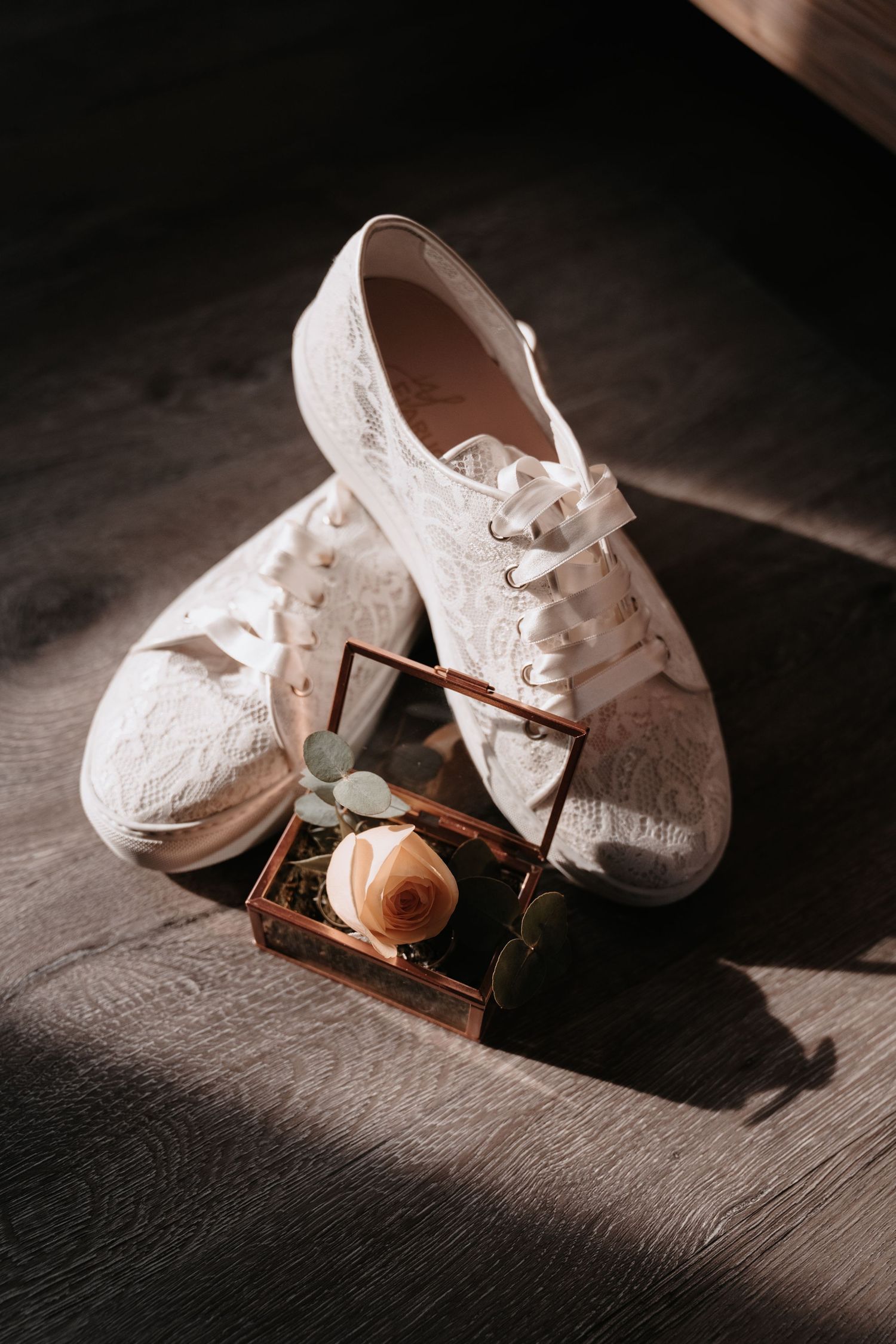 White lace bridal sneakers and hourglass on wooden surface in moody lighting.