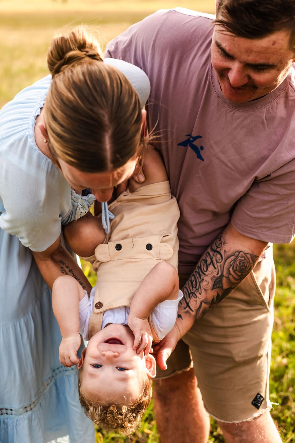 Joyful family playing together outdoors as they hold their laughing child upside down.