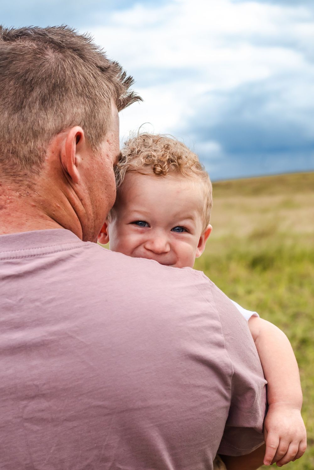 Sweet candid moment of a child smiling over someone's shoulder in an outdoor setting.