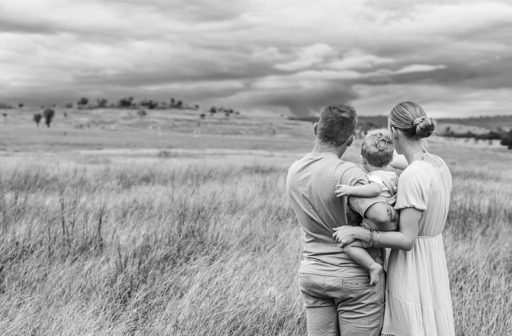 Black and white portrait of a family standing together in a scenic grassland landscape.