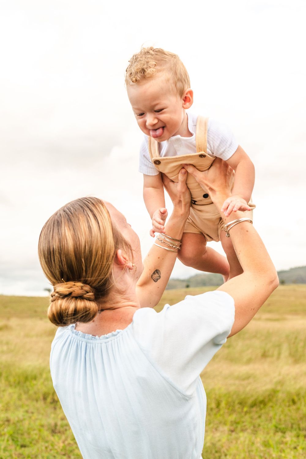 Playful moment captured as a child is lifted high into the air in a grassy field.