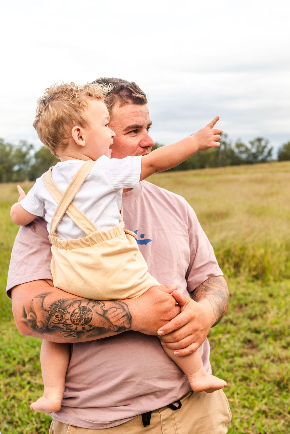 A touching outdoor moment with someone holding a child in overalls pointing at something in the distance.