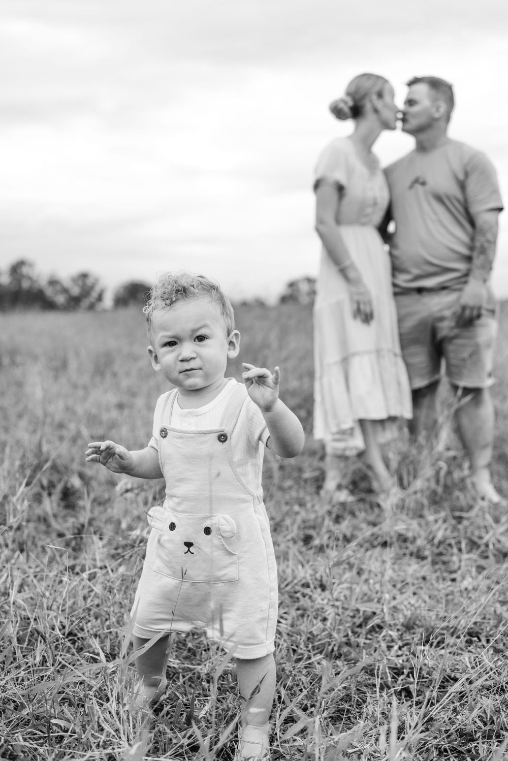 A series of candid black and white photos showing a toddler walking in a grassy field.