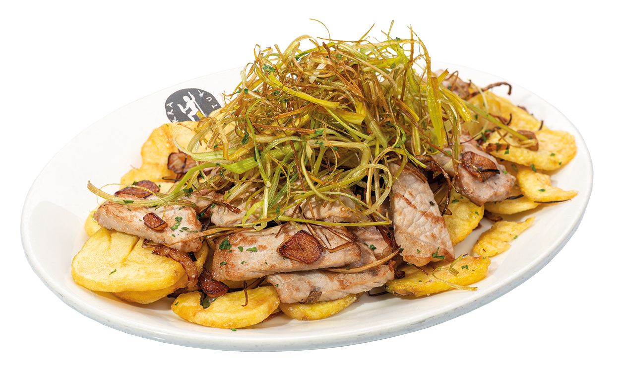 Carne de cerdo en rodajas finas con gajos de patatas fritas crujientes cubiertas con cebolletas ralladas en un plato ovalado. Tierra Astur