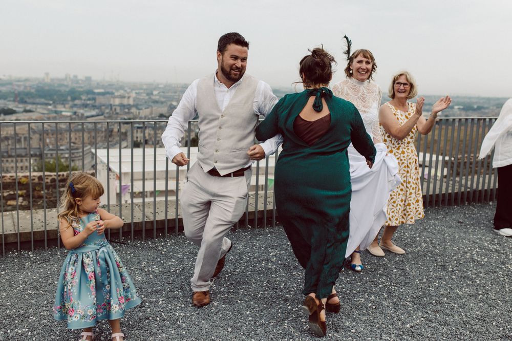 Wedding party celebrates with champagne on scenic overlook of Edinburgh city skyline.