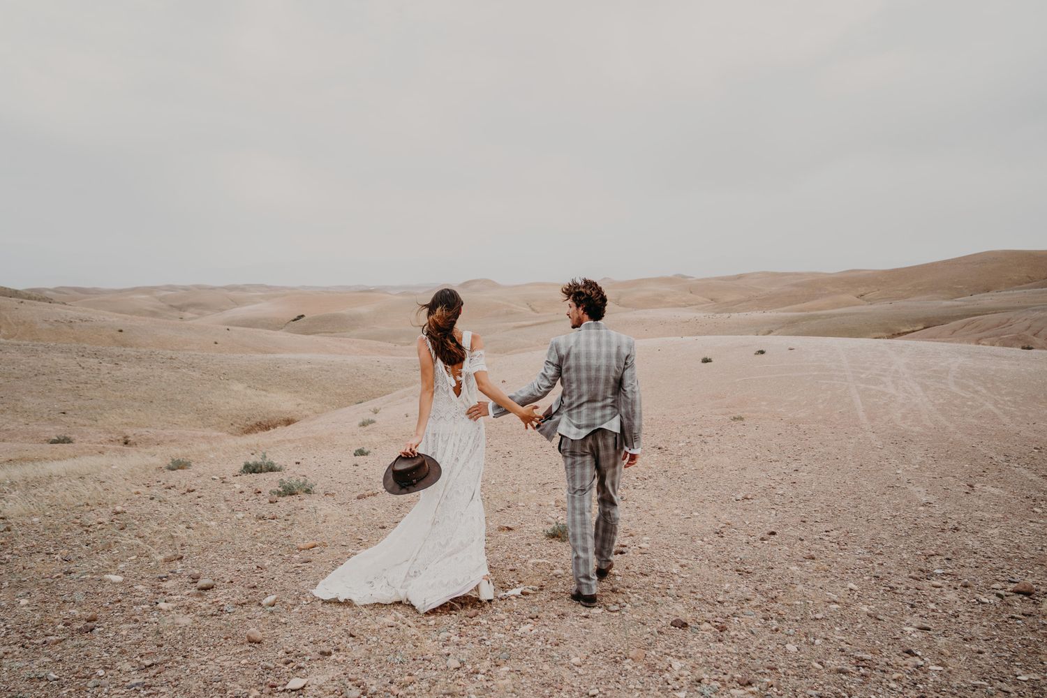 Newlyweds hold hands while standing in scenic desert setting.