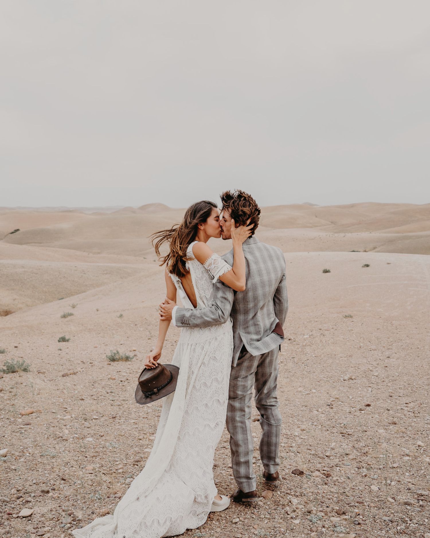 Couple in wedding attire sharing intimate moment in desert landscape.