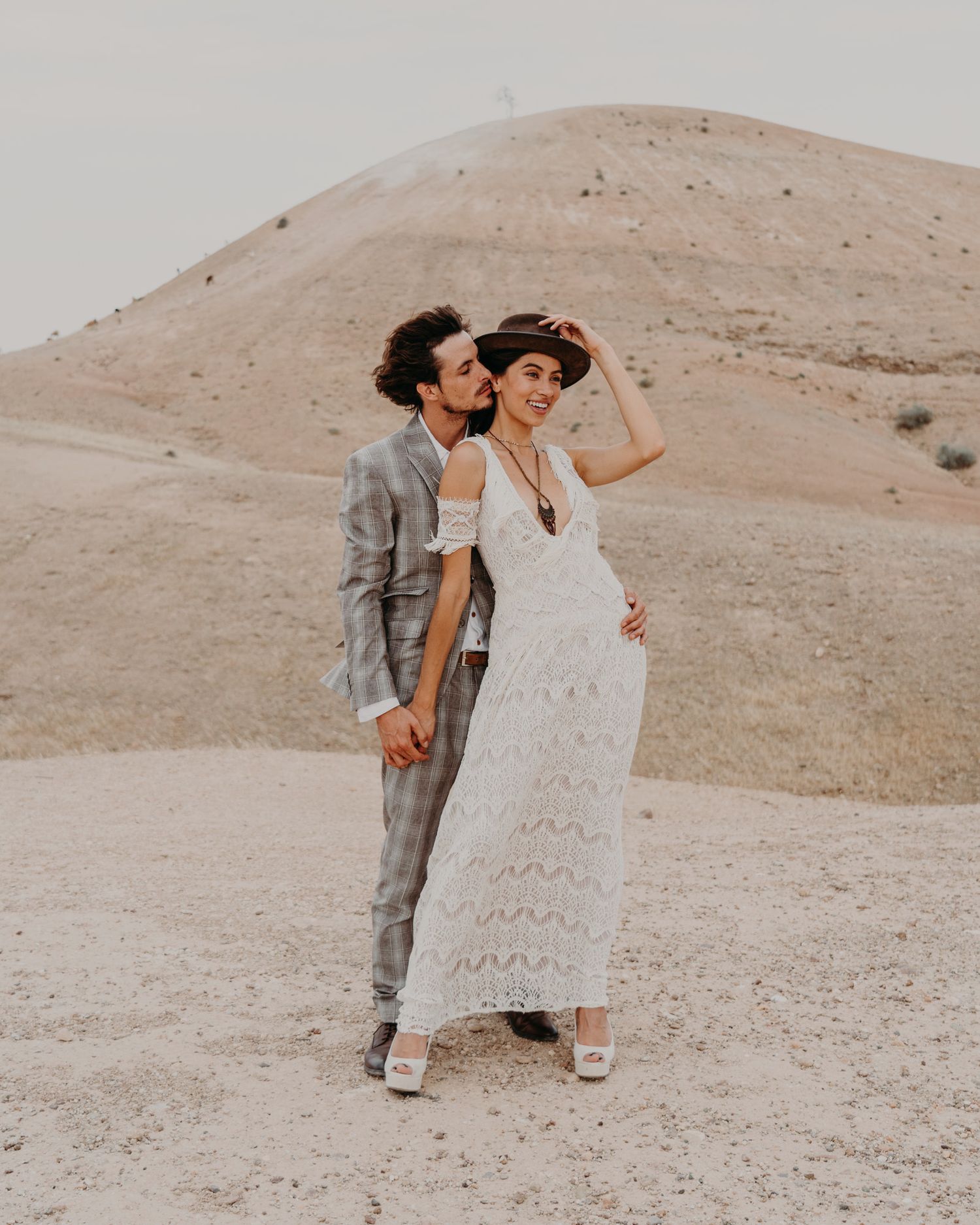 Stylish desert wedding portrait with couple against sand dunes.