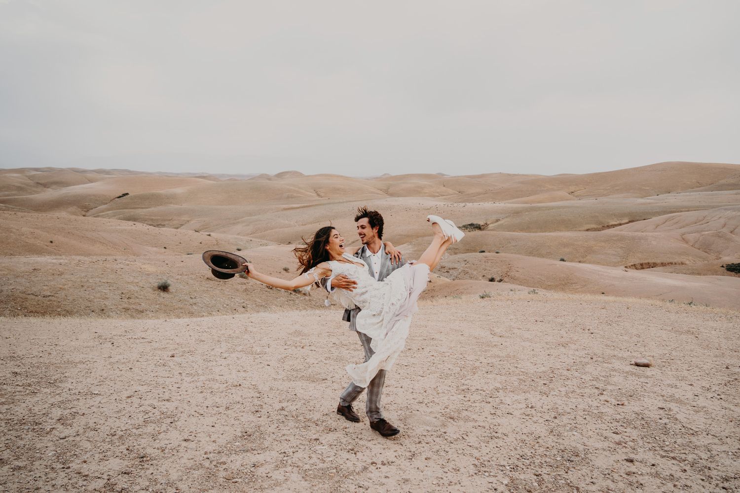 Playful wedding couple dancing in desert landscape.