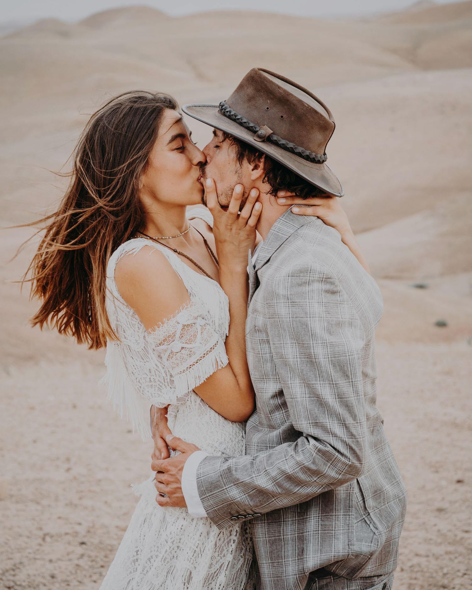 Intimate desert wedding kiss captured in warm evening light.
