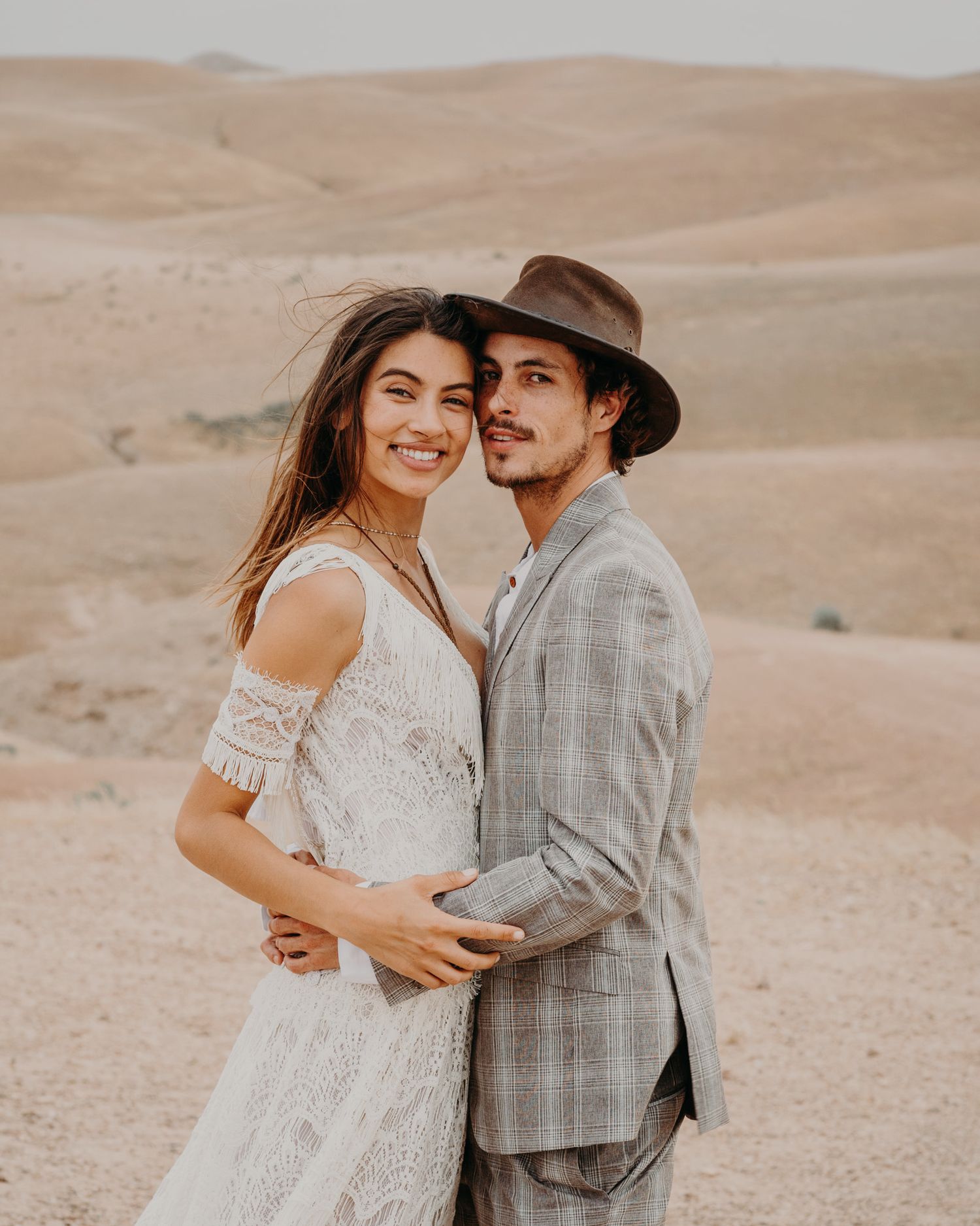 A romantic desert photoshoot featuring a couple in formal attire embracing among sand dunes.