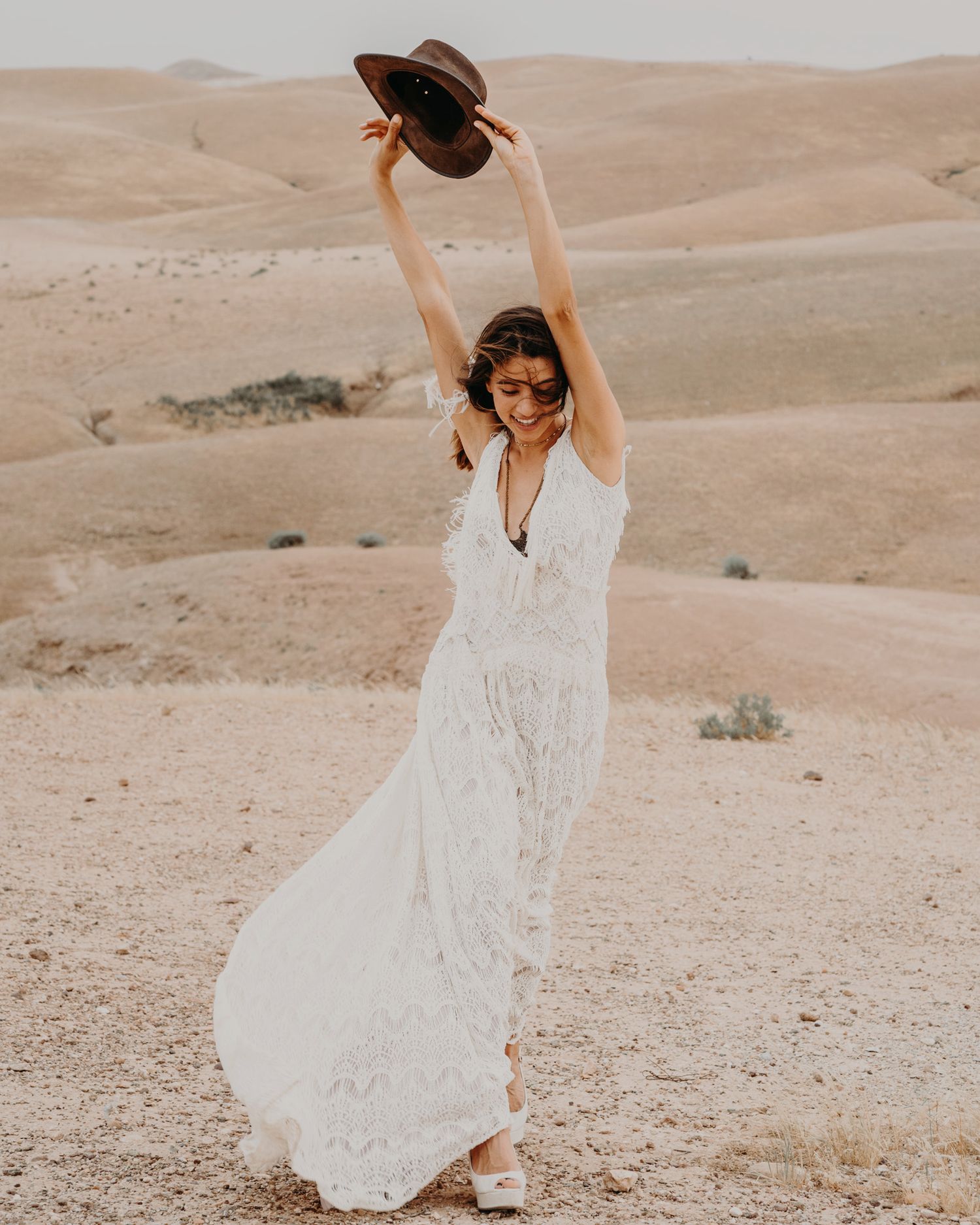 A free-spirited dance pose with a white dress against sandy desert hills.