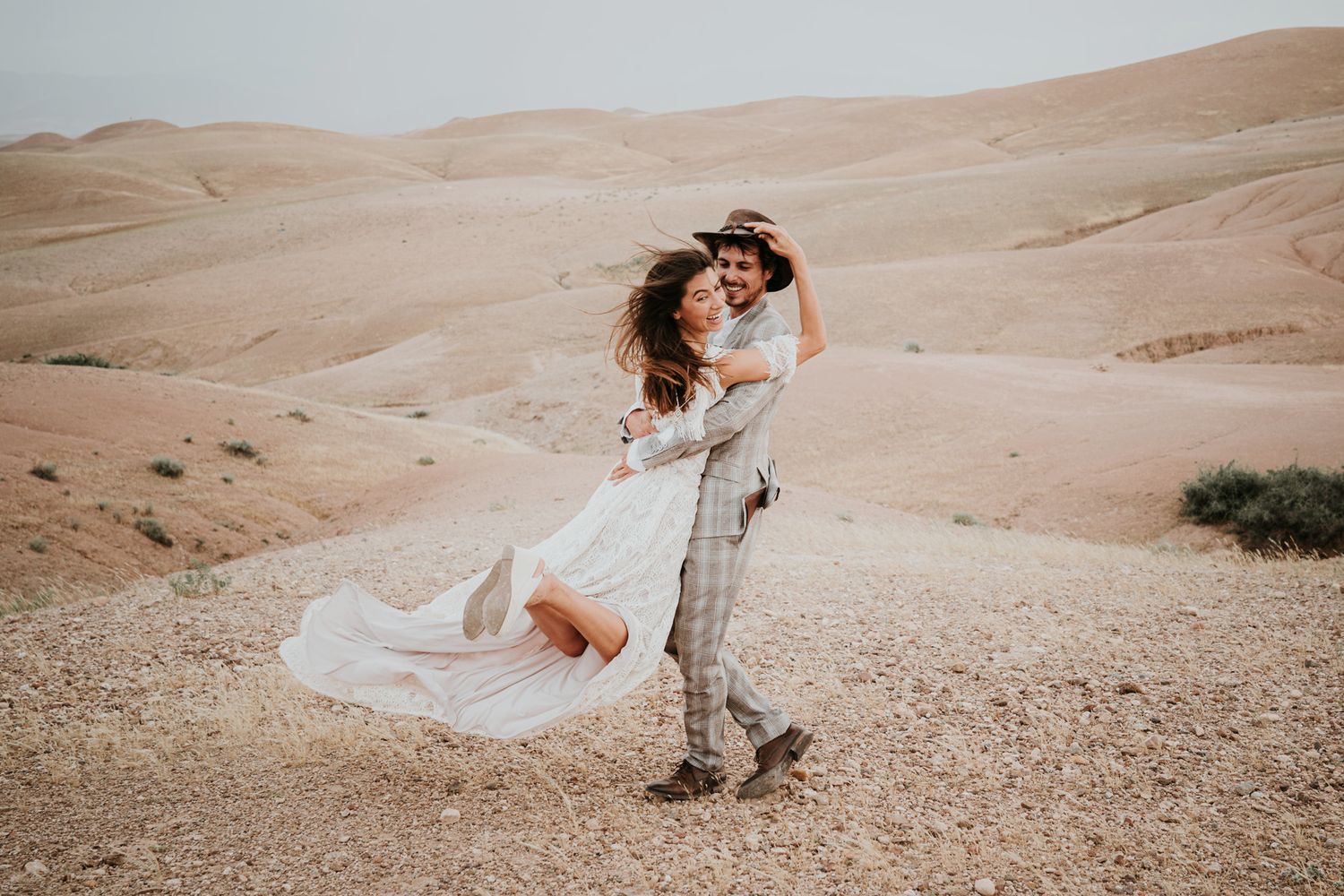 A romantic desert embrace with flowing white dress and checkered suit.