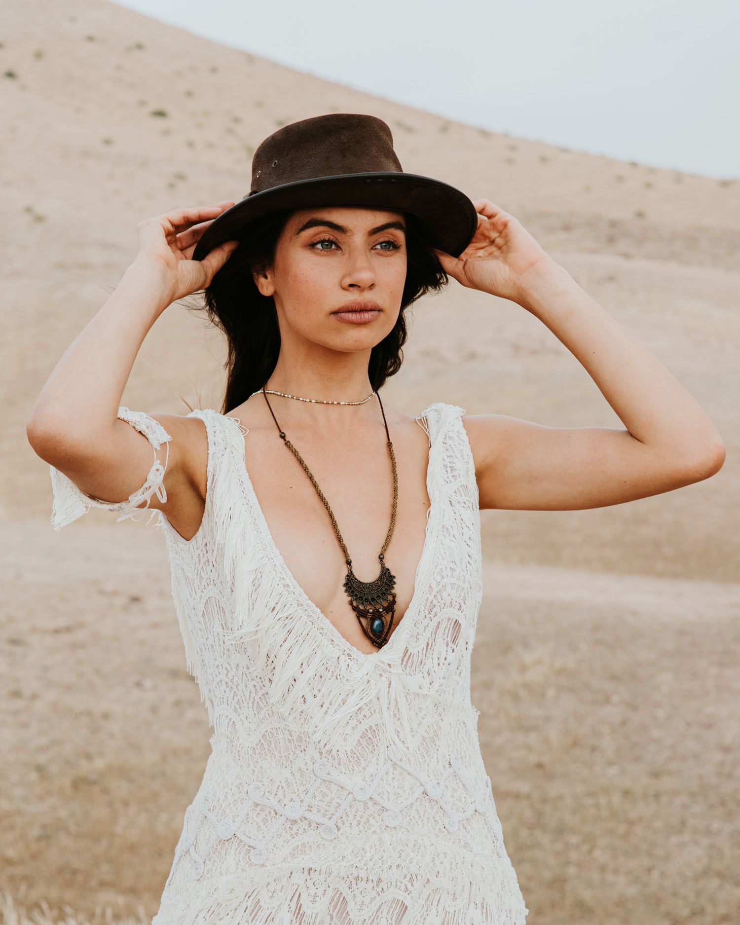 A bohemian desert portrait featuring a white lace dress and brown hat.