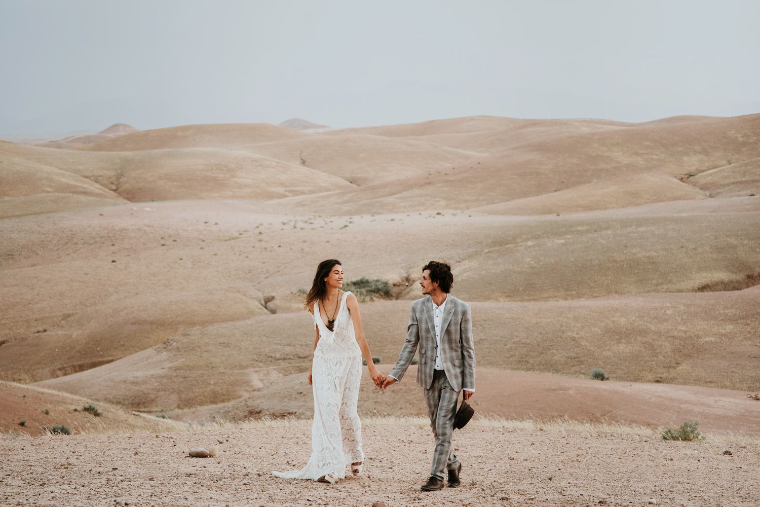A couple enjoys an intimate moment in a desert landscape with rolling sand dunes in the background.