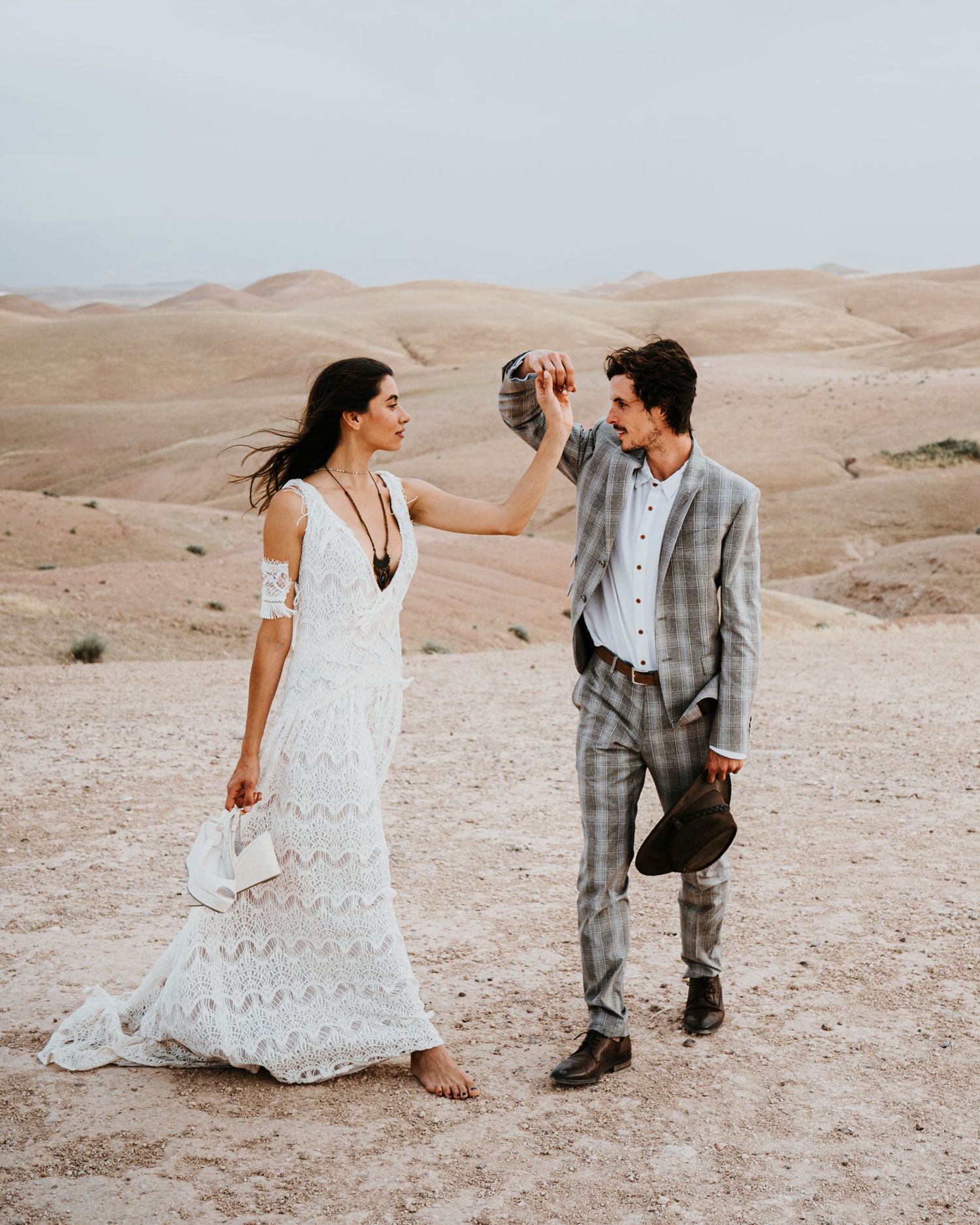 A couple dances together in the desert wearing formal attire against sandy hills.