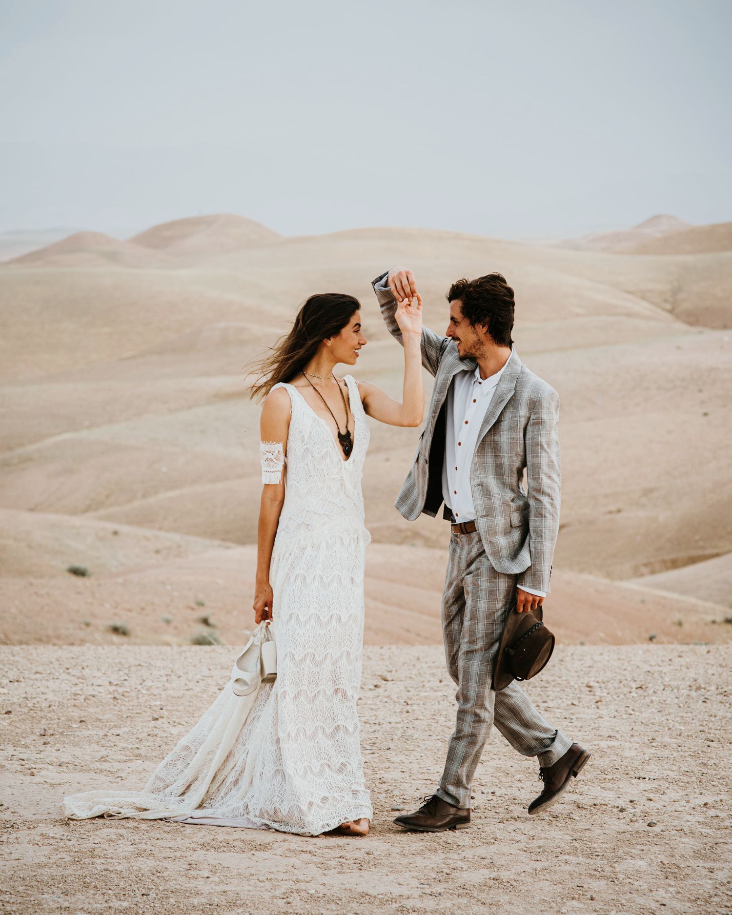 A couple dances together in elegant attire against a backdrop of desert hills.