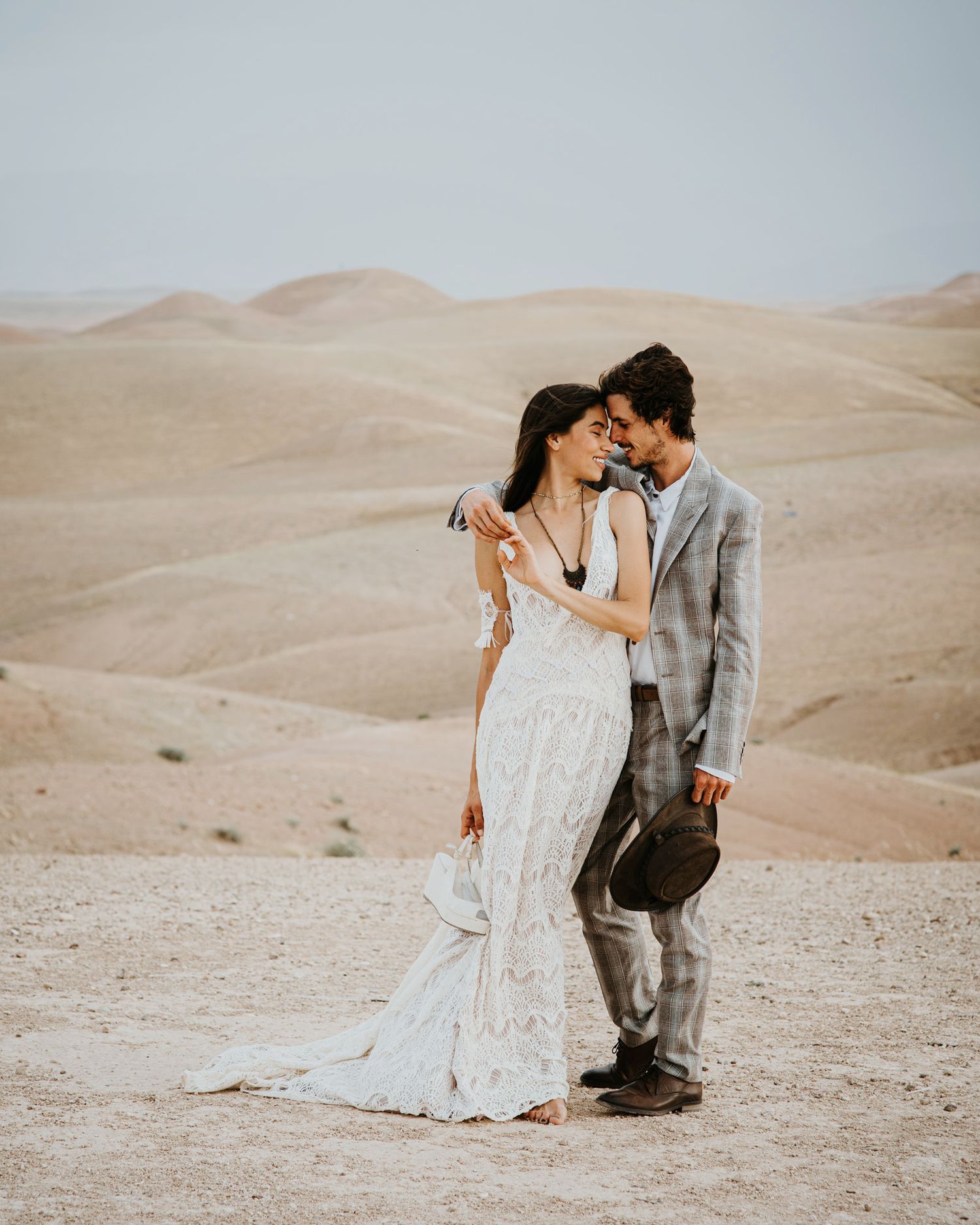 A couple shares an intimate moment against rolling desert hills in wedding attire.