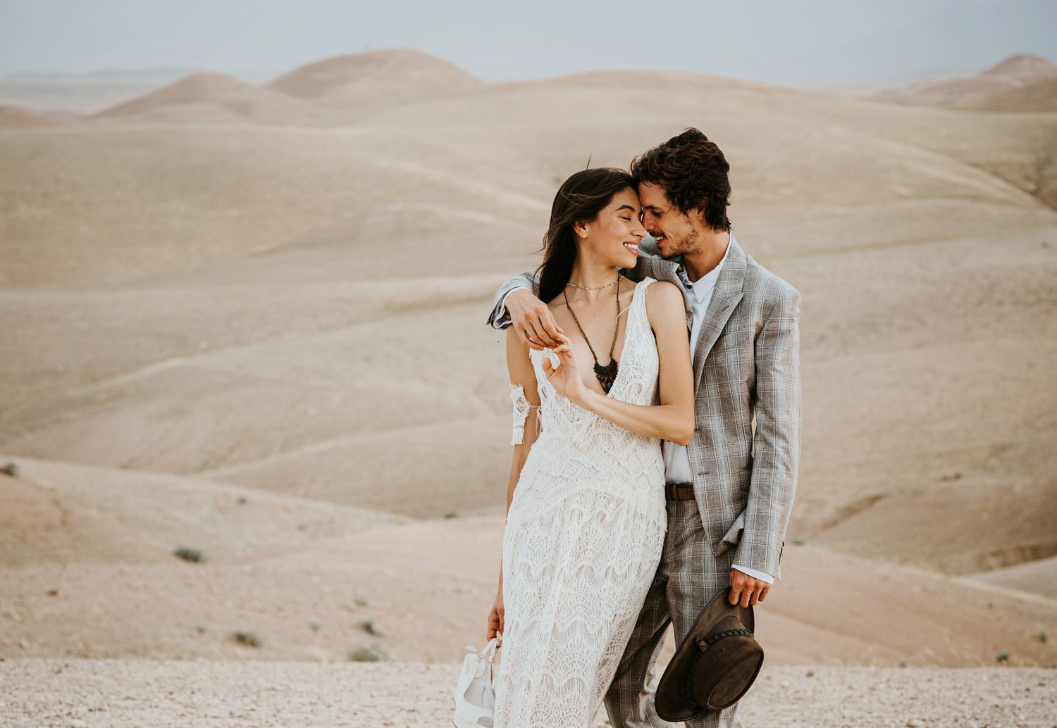A tender embrace between a couple in formal wear with desert dunes in the background.