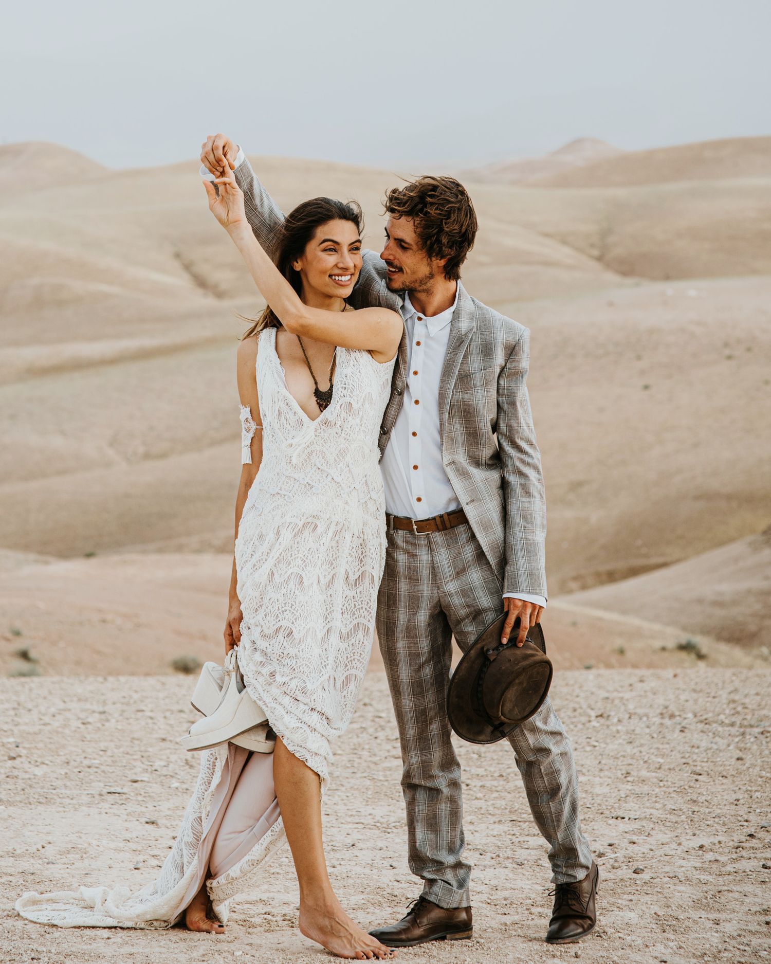 A joyful dancing moment between a couple in wedding attire in a desert setting.