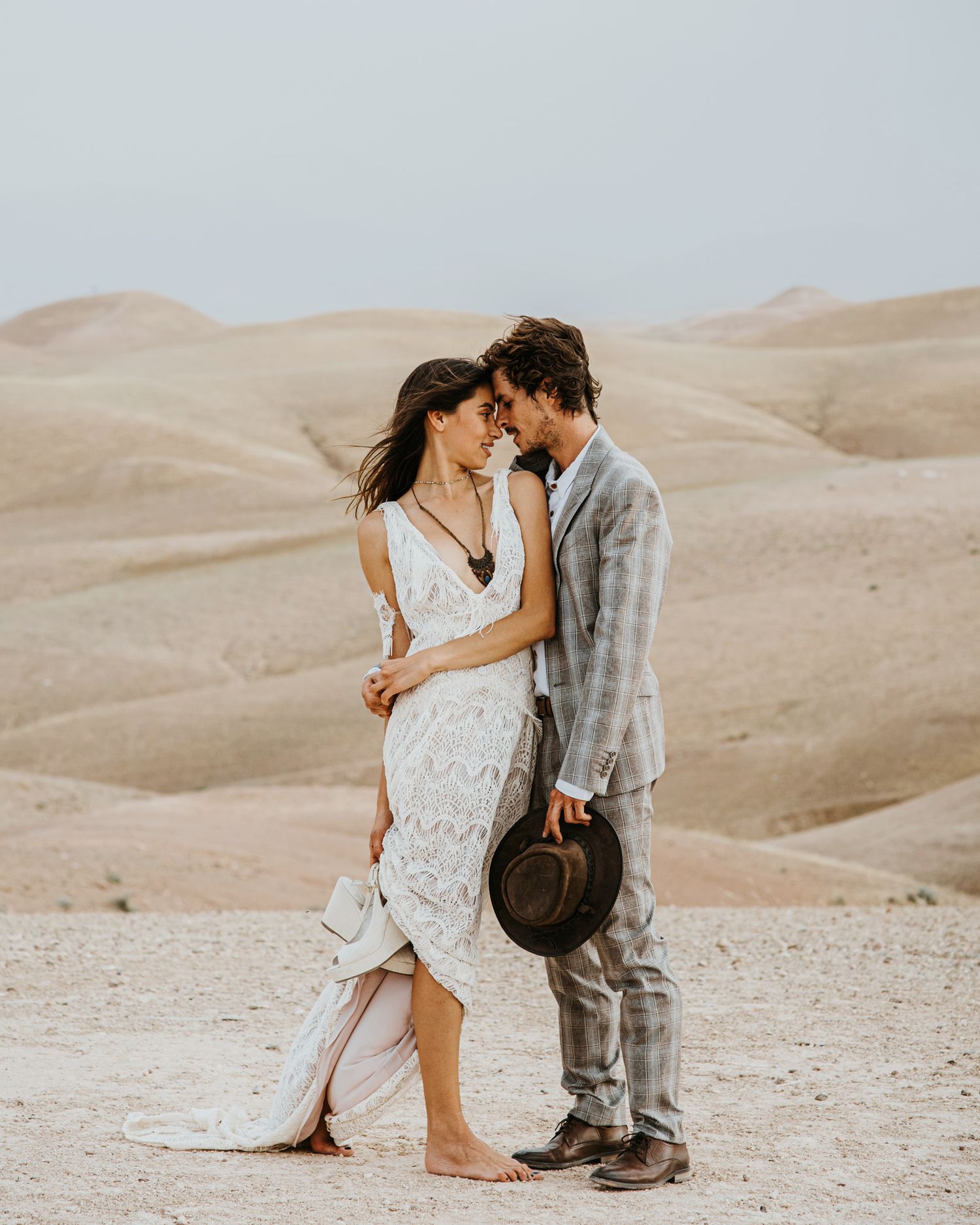 A romantic desert portrait of a couple in wedding attire against sandy hills.