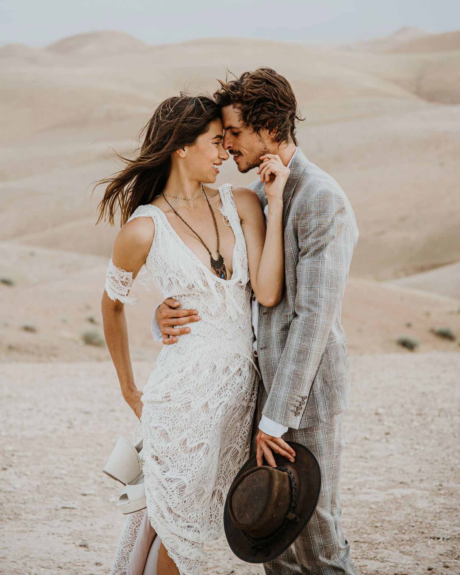 Intimate desert portrait of couple in wedding attire sharing tender moment against sand dunes background.