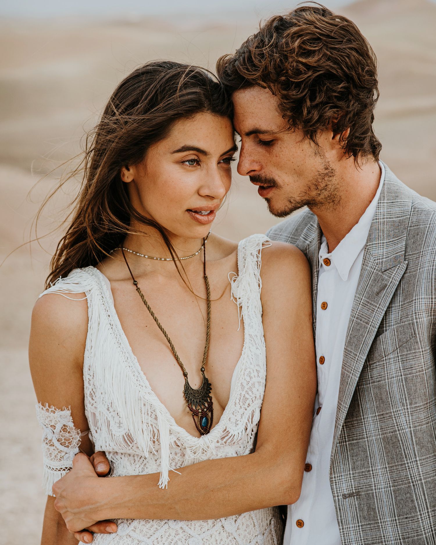 Close up desert portrait of couple in bohemian wedding attire with dramatic sand dunes backdrop.