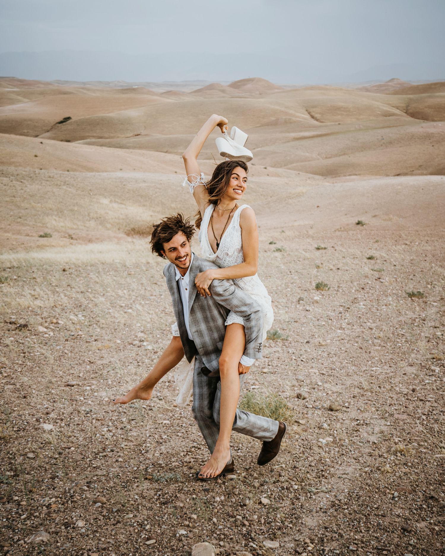 Candid desert wedding photo showing playful couple against rolling sand dunes backdrop.