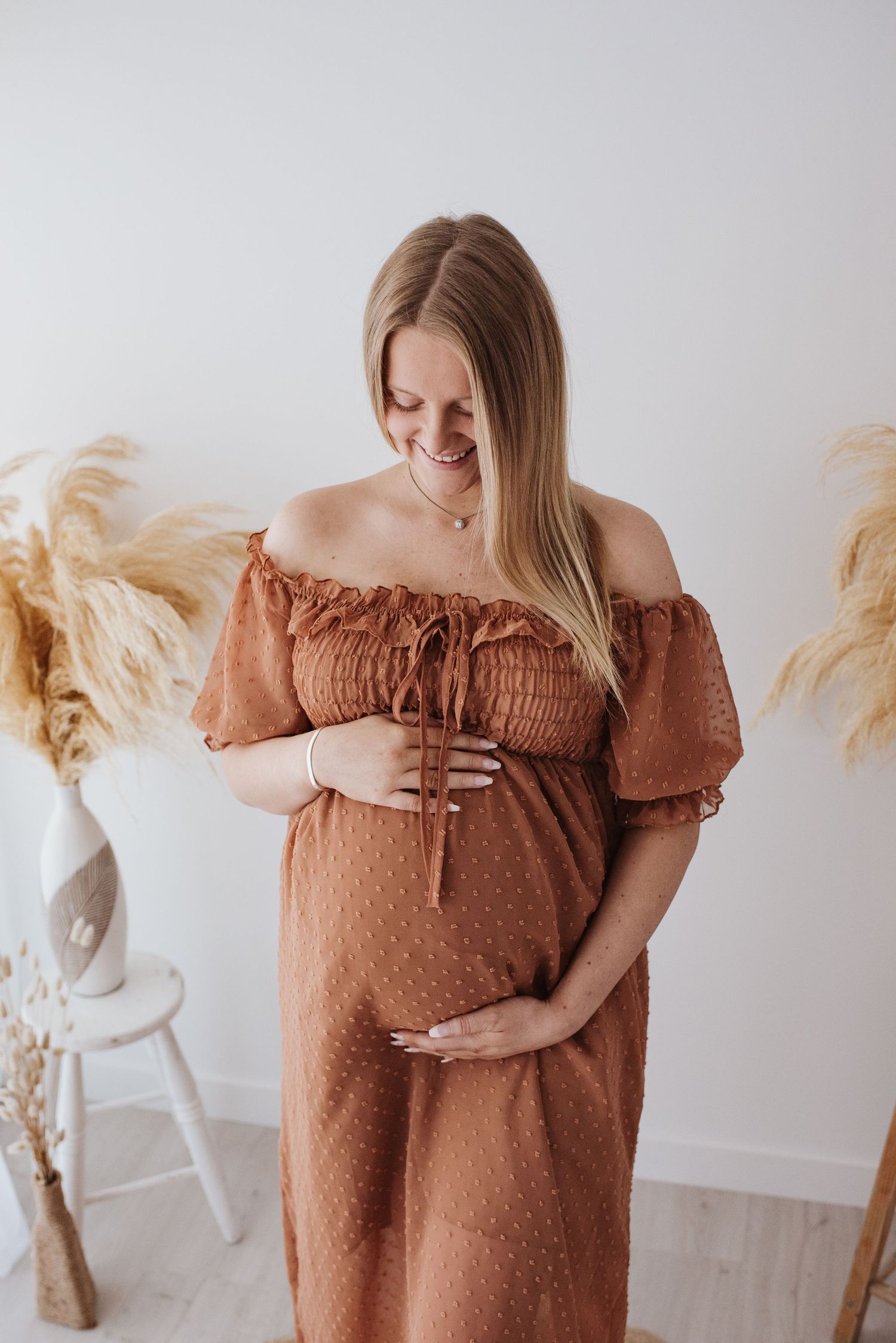 Cozy indoor maternity photo with pampas grass decor and terracotta dress.