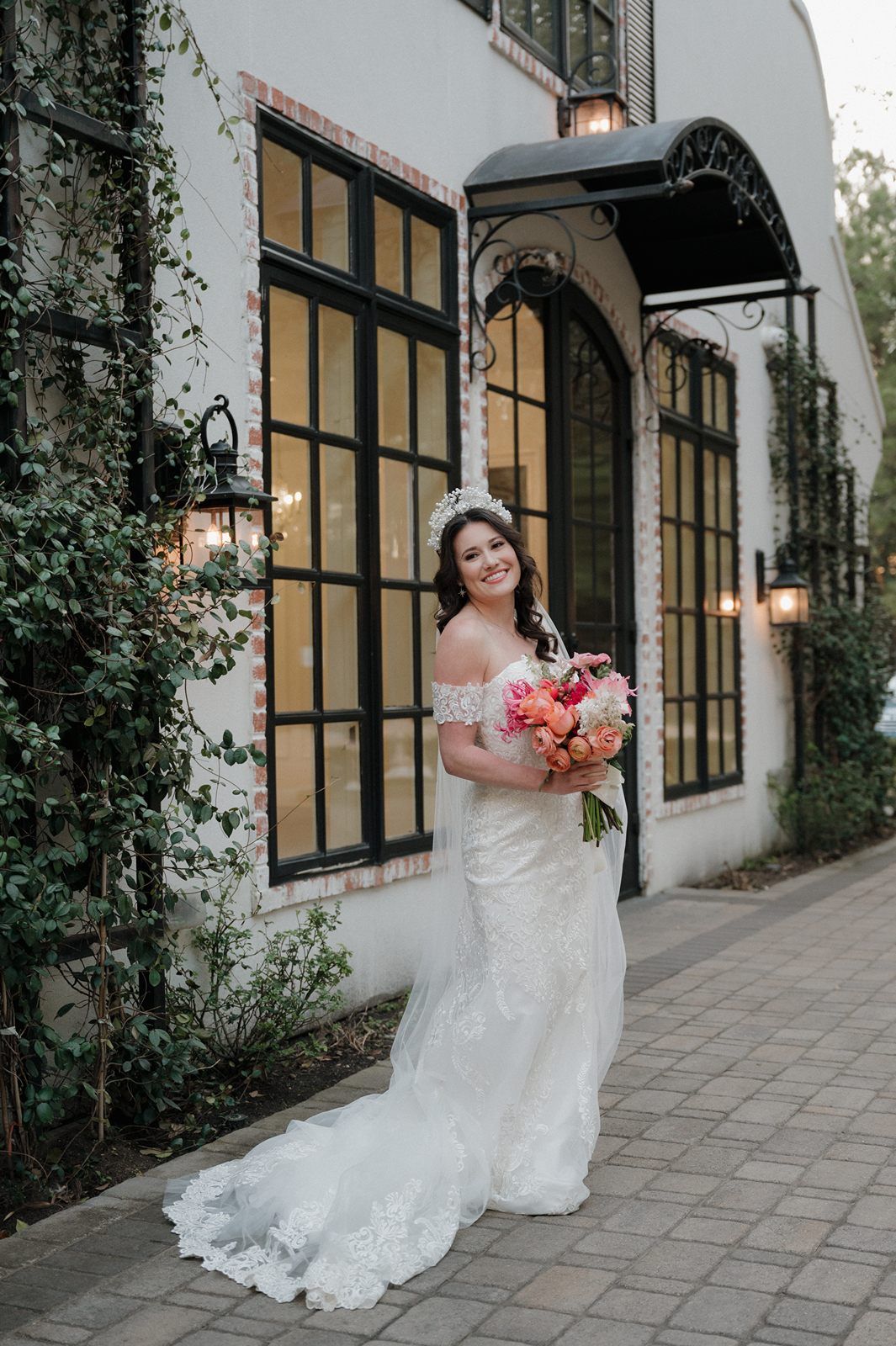 White bridal wedding gown with lace detail and train photographed at elegant venue with arched doorway and climbing vines.
