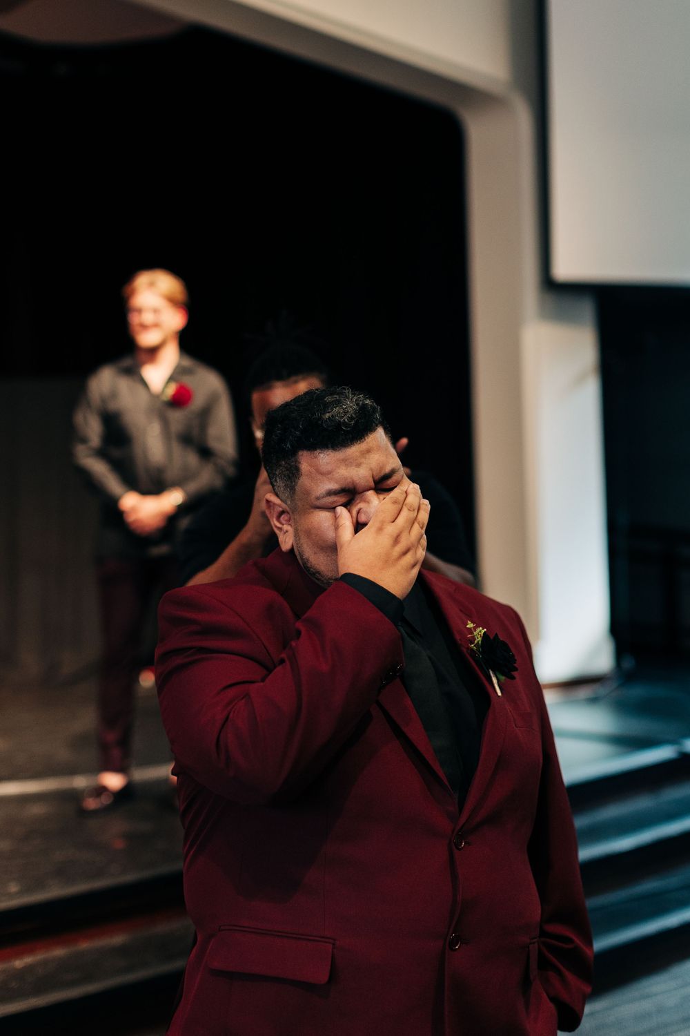 A person in a burgundy suit shows emotion during a wedding ceremony.