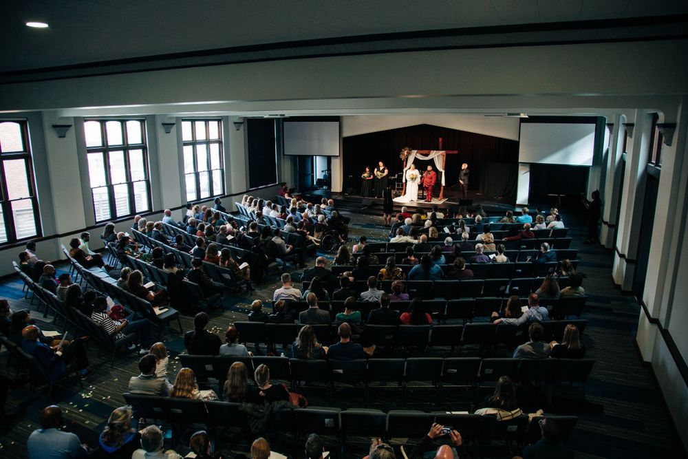 A wide view of a wedding ceremony in a large hall filled with guests seated in rows.