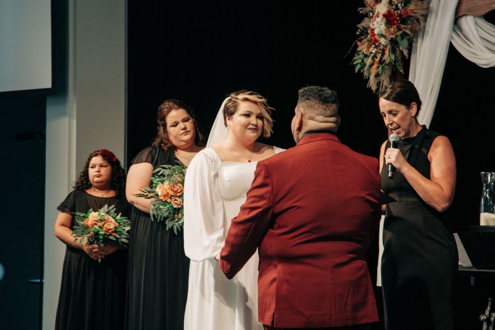 A wedding ceremony scene with attendants in dark formal wear under elegant lighting.