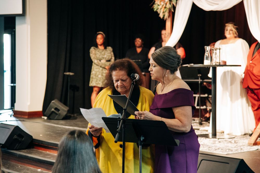 Wedding ceremony participants reading from papers during an indoor service with stage lighting.