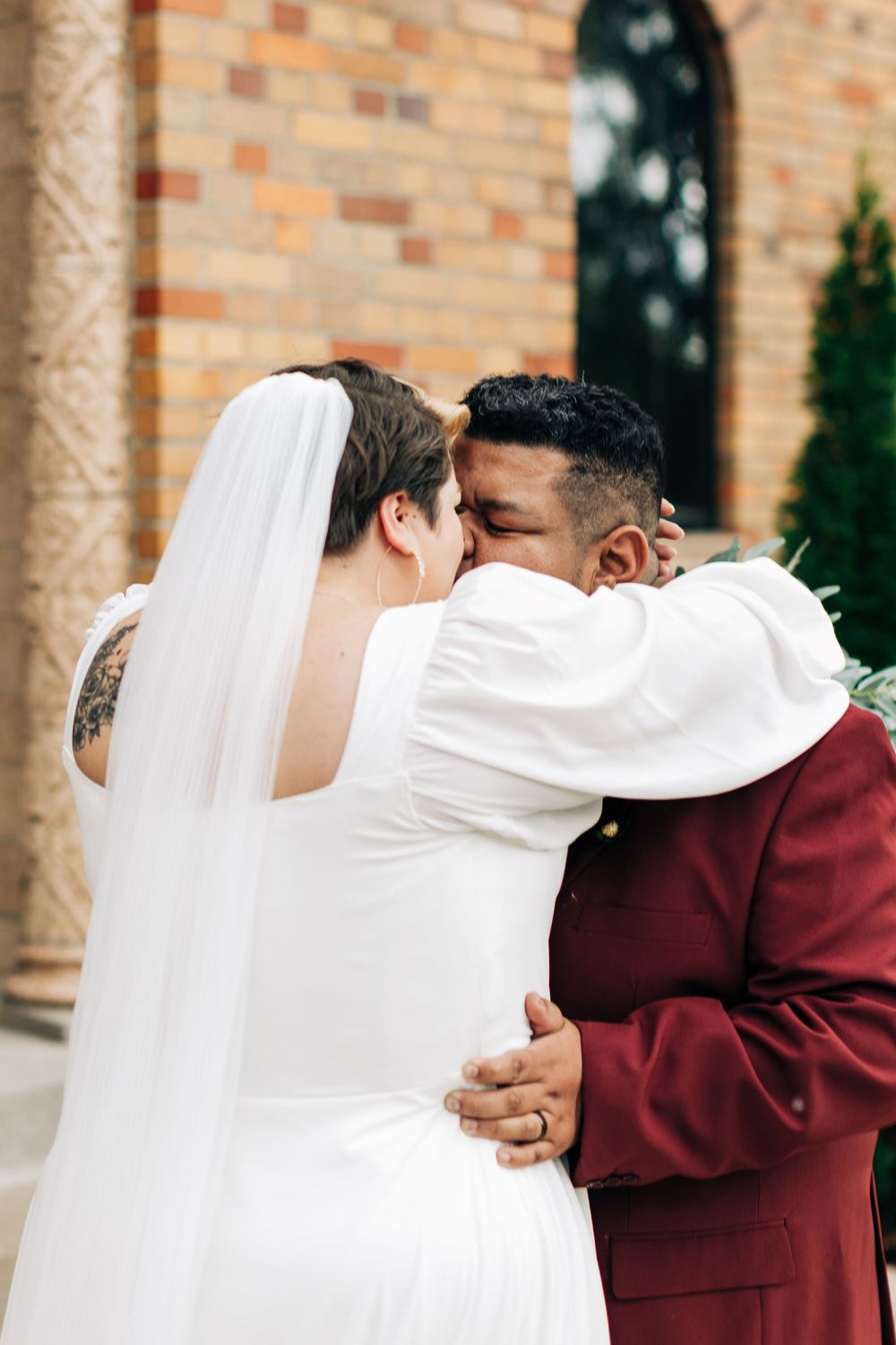 A romantic wedding moment shared between newlyweds outside a brick church.